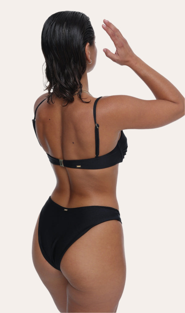 Amour black bikini Bottoms in Onyx with a gold ring, Sustainable recycled swimwear luxury bikini, seen on a model raising both arms to her face
