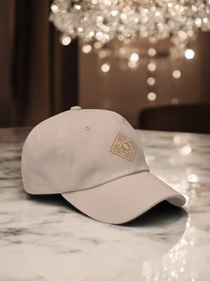 beige embroidered luxury cap with oumaima swim logo, seen on a marble counter with chandelier in the background