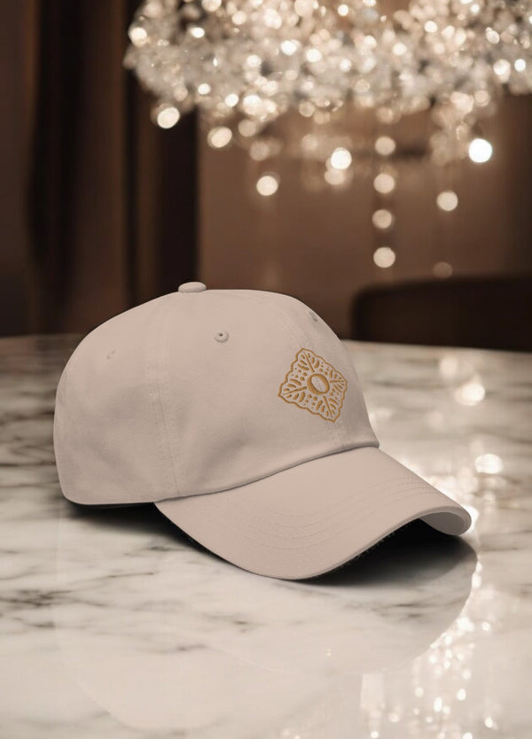 beige embroidered luxury cap with oumaima swim logo, seen on a marble counter with chandelier in the background