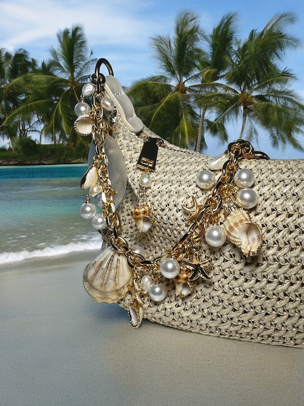 Chain shell beach bag evening bag with pearls and shells charms gold beige Oumaima swim, seen on the beach with palm tree background